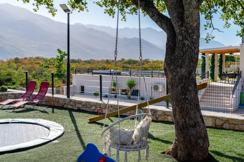 Garden swing beneath a tree beside the trampoline and playground