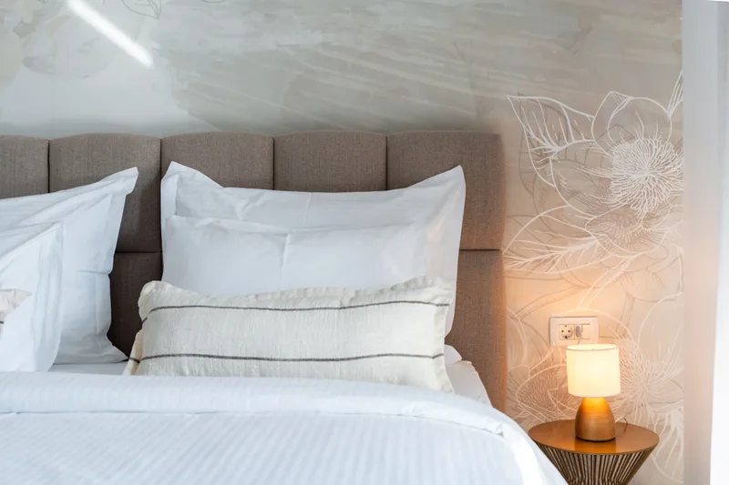 Upholstered double bed with white linen and bedside lighting