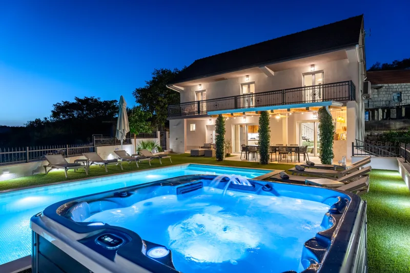 Illuminated Jacuzzi with the pool and lit villa behind it at dusk